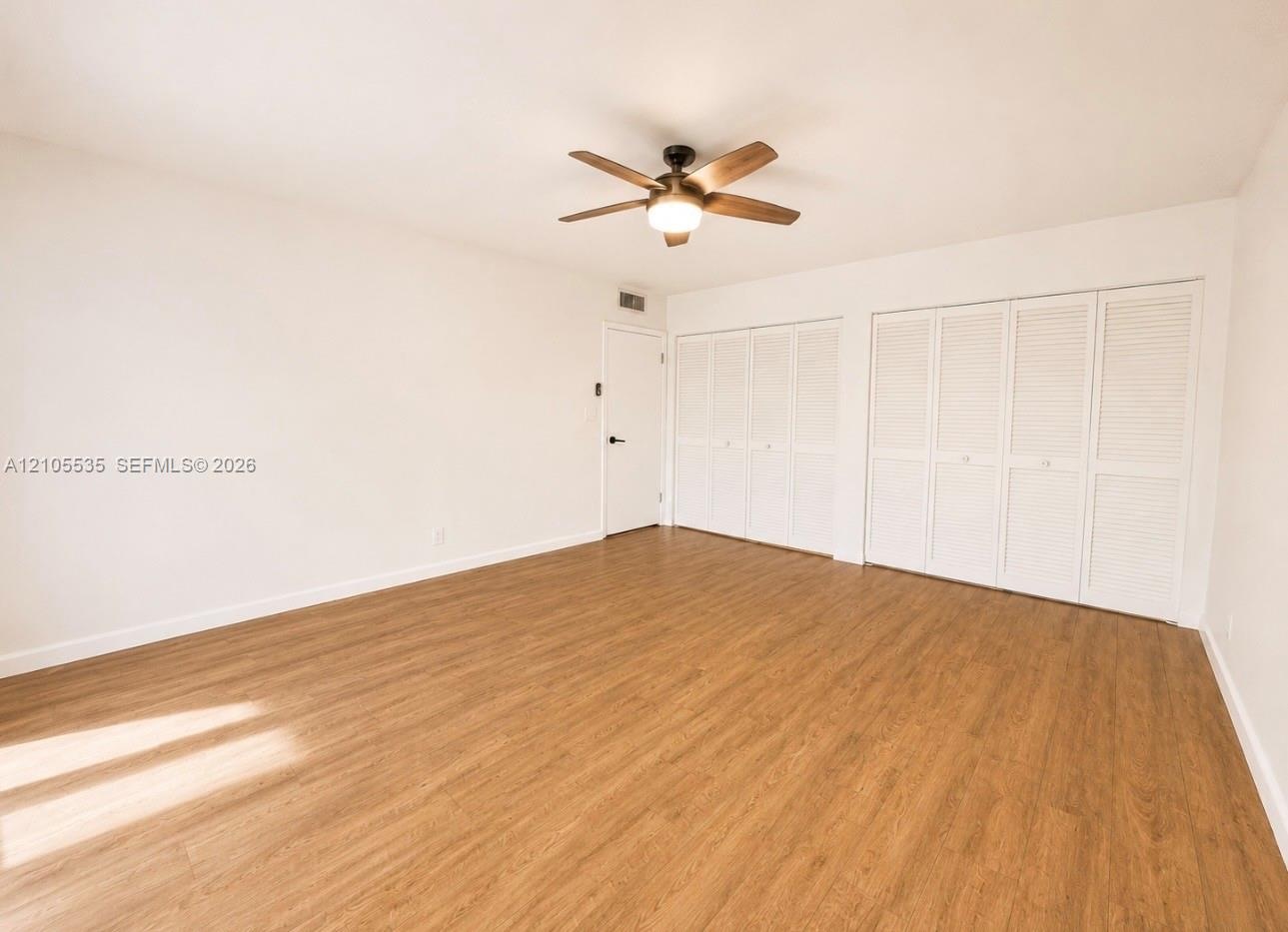 Wood-finish flooring, ceiling fan with integrated lighting, and multiple louvered bifold closet doors