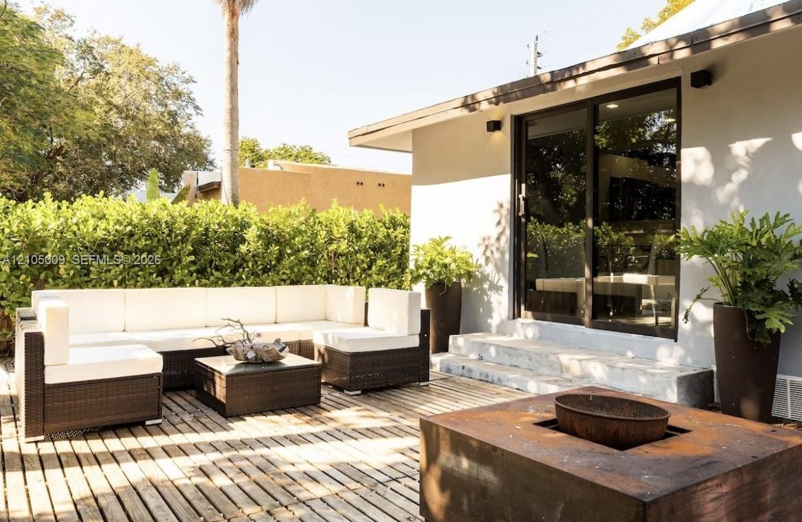Exterior wood deck with a built-in fire pit, privacy hedging, concrete steps, and dark-framed sliding glass doors