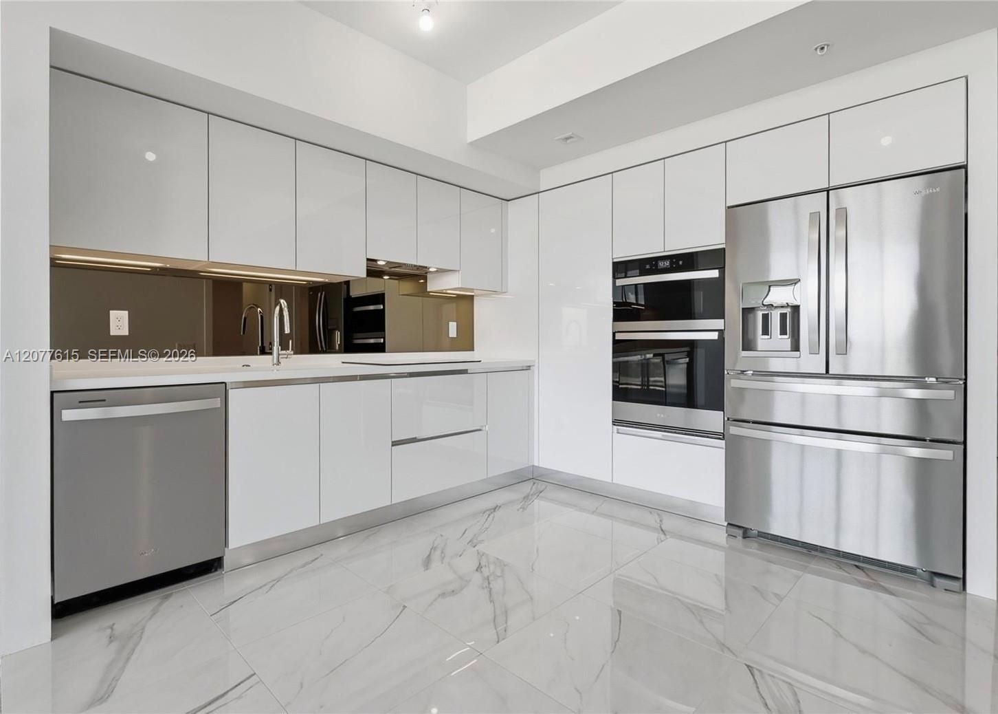 Sleek kitchen featuring white flat-panel cabinetry, stainless steel appliances, a mirrored backsplash, and large format tile flooring