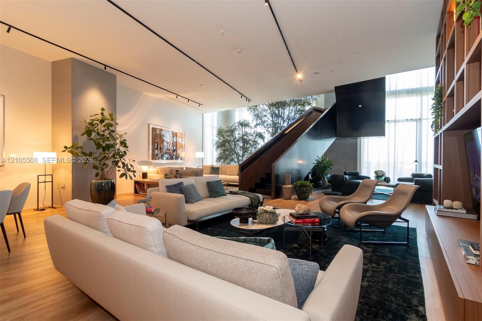 Expansive open-concept living area with wood-finish flooring, high ceilings, built-in shelving, and a prominent staircase with dark wood-finish treads