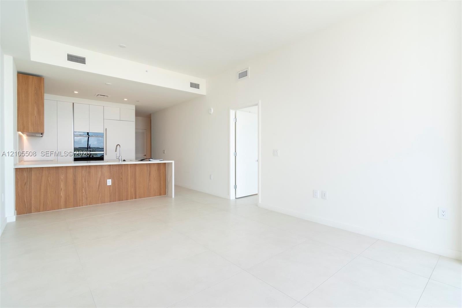 Open-concept living space featuring high ceilings, light tile flooring, built-in kitchen cabinetry with integrated appliances, and a kitchen island wi