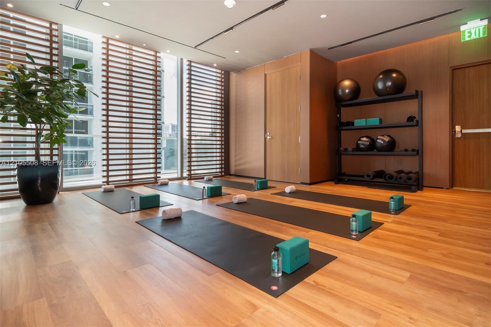 Wood-finish flooring, full-height windows with horizontal blinds, wood-paneled walls, and built-in exercise equipment storage