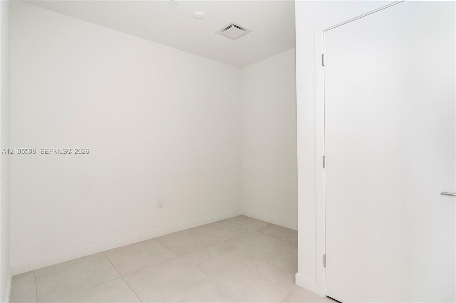 White ceramic tile flooring, recessed ceiling lighting, and a flush-mounted door with a modern handle