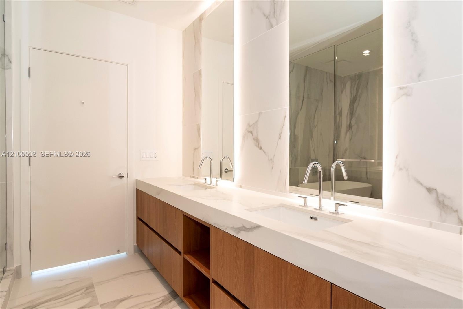 Dual undermount sinks with chrome faucets, integrated vanity lighting, and wood-finish cabinetry