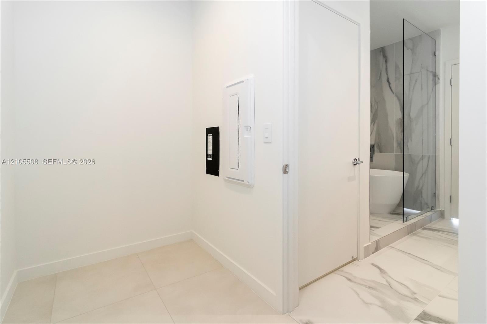 White interior walls, light-toned tile flooring, and a glass-enclosed shower with a marble-patterned tile surround