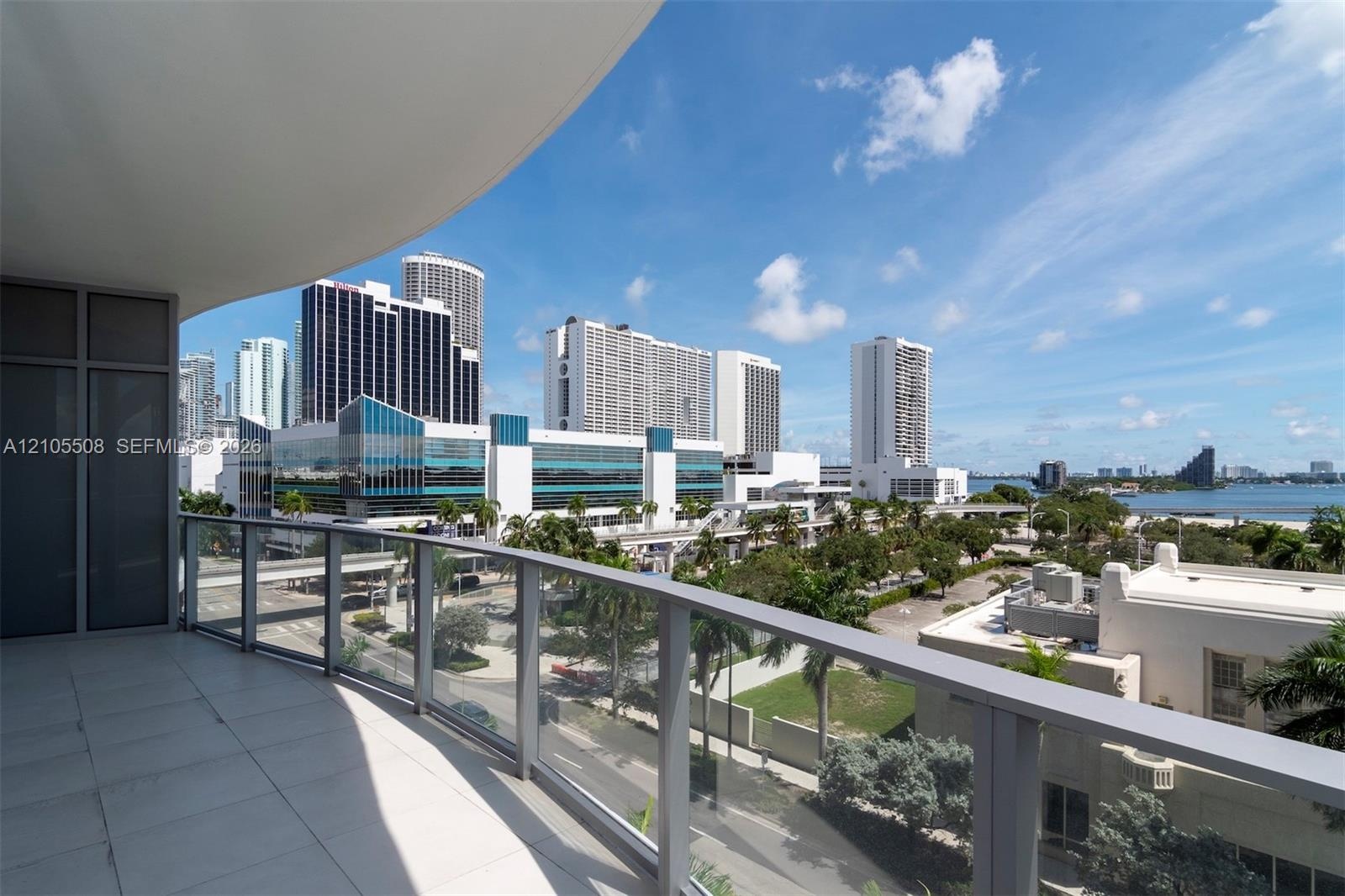 Curved balcony with glass railing, tile flooring, and urban skyline with water backdrop