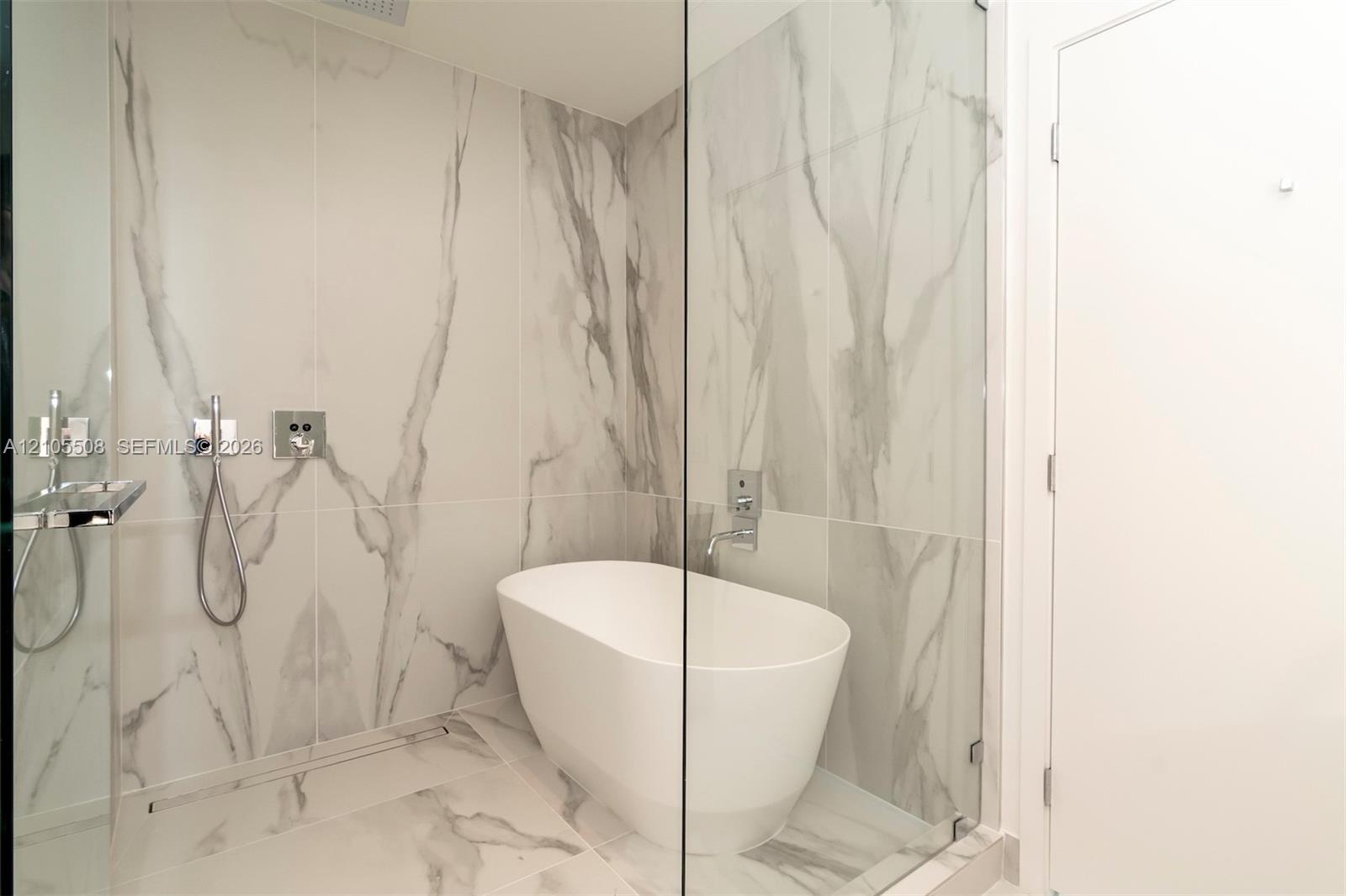 Freestanding tub within a glass-enclosed shower, featuring large format wall and floor tiling, and polished chrome fixtures