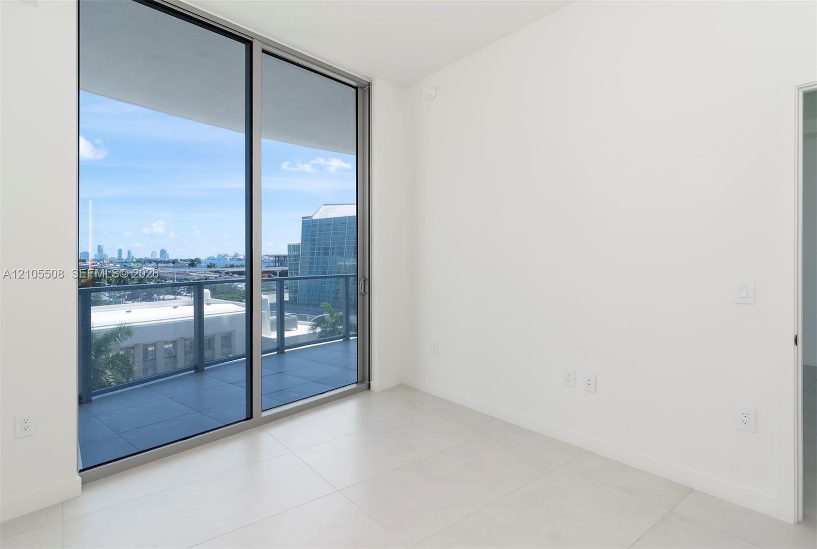 Expansive sliding glass doors, balcony with glass railing, light tile flooring, and white walls