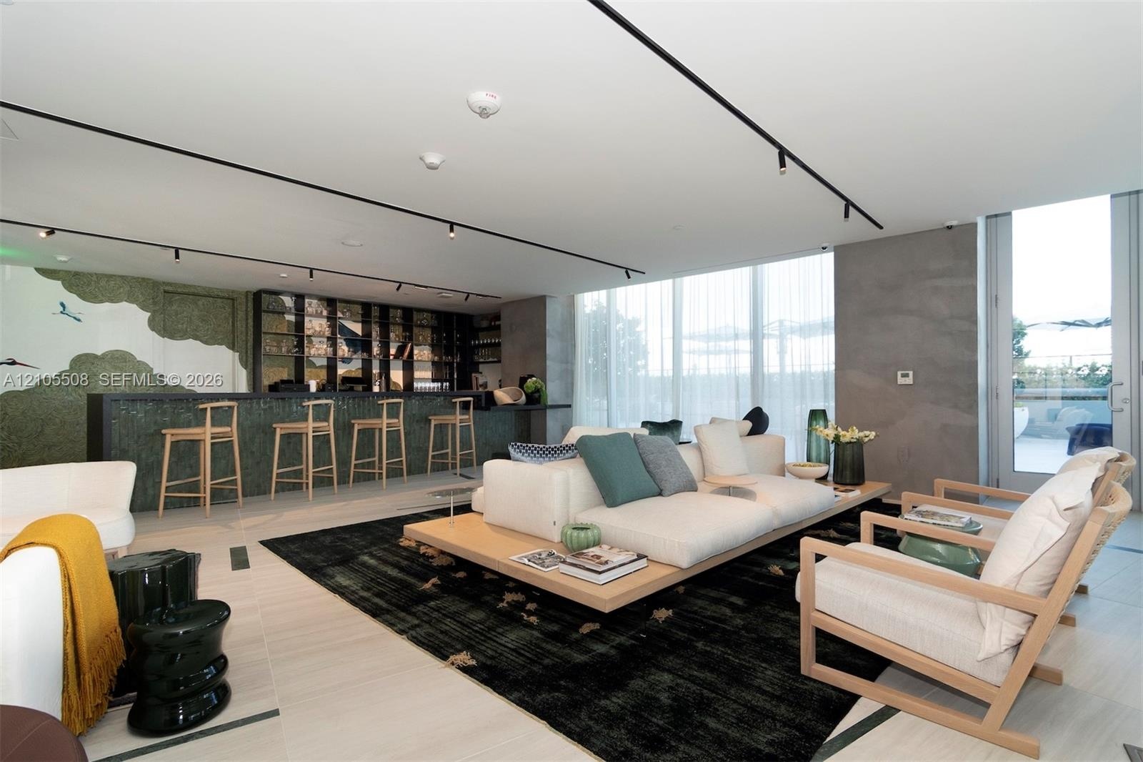 Integrated wet bar with barstool seating, recessed track lighting, full-height windows with sheer window treatments, concrete accent wall, and light-t