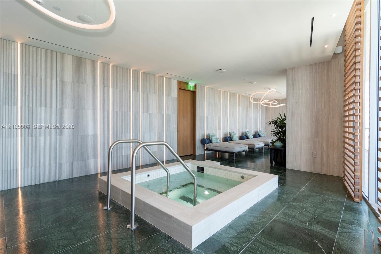 Square hot tub with stainless steel railings, set into dark green tiled flooring