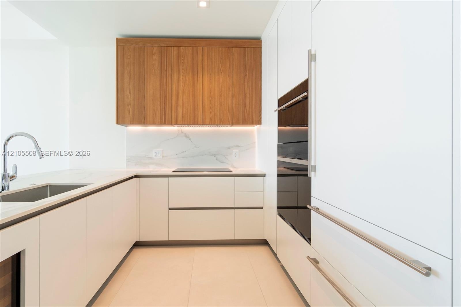 Sleek kitchen featuring light-toned cabinetry, wood-finish upper cabinets, integrated appliances, a built-in cooktop, and a stainless steel sink