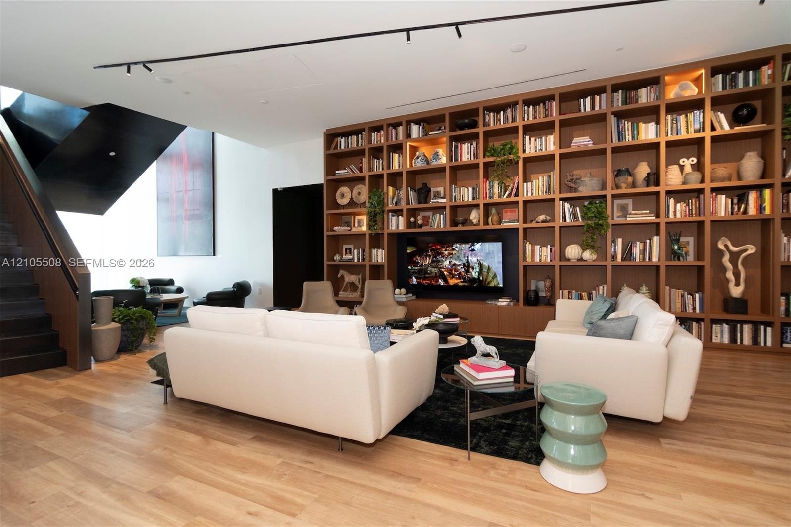 Expansive living area featuring wood-finish flooring, a full-height built-in bookshelf wall with integrated television, and a dark-finished open stair