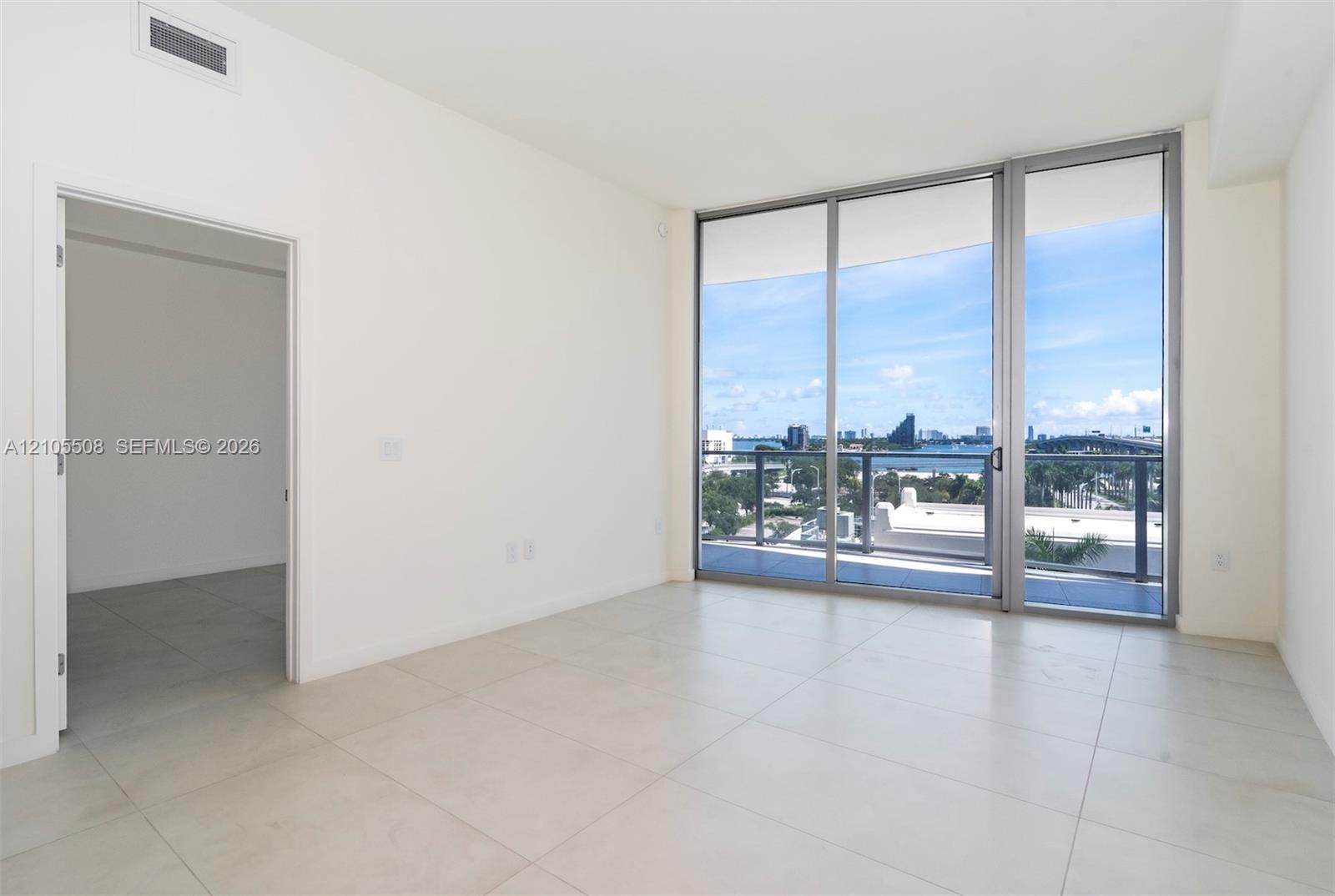 Sliding glass doors opening to a balcony with metal railings, tile flooring, and white walls