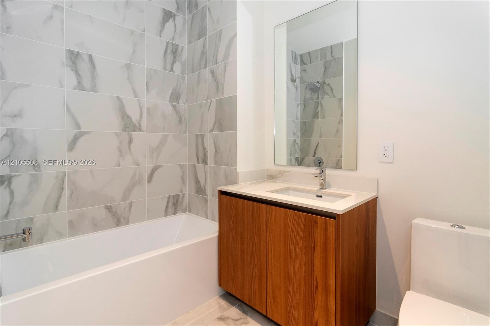 Bathtub with subway tile surround, wood-finish vanity with countertop, and rectangular wall-mounted mirror