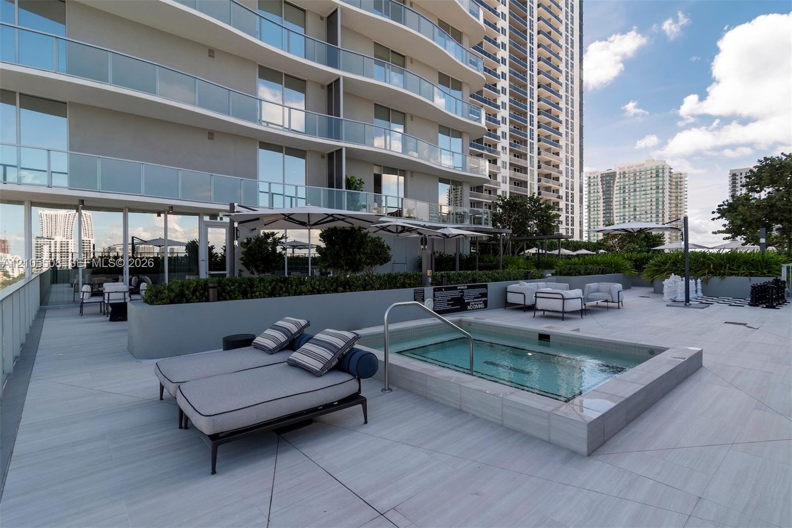 Rooftop amenity deck featuring a built-in spa, expansive tiled patio, and integrated planters with mature landscaping