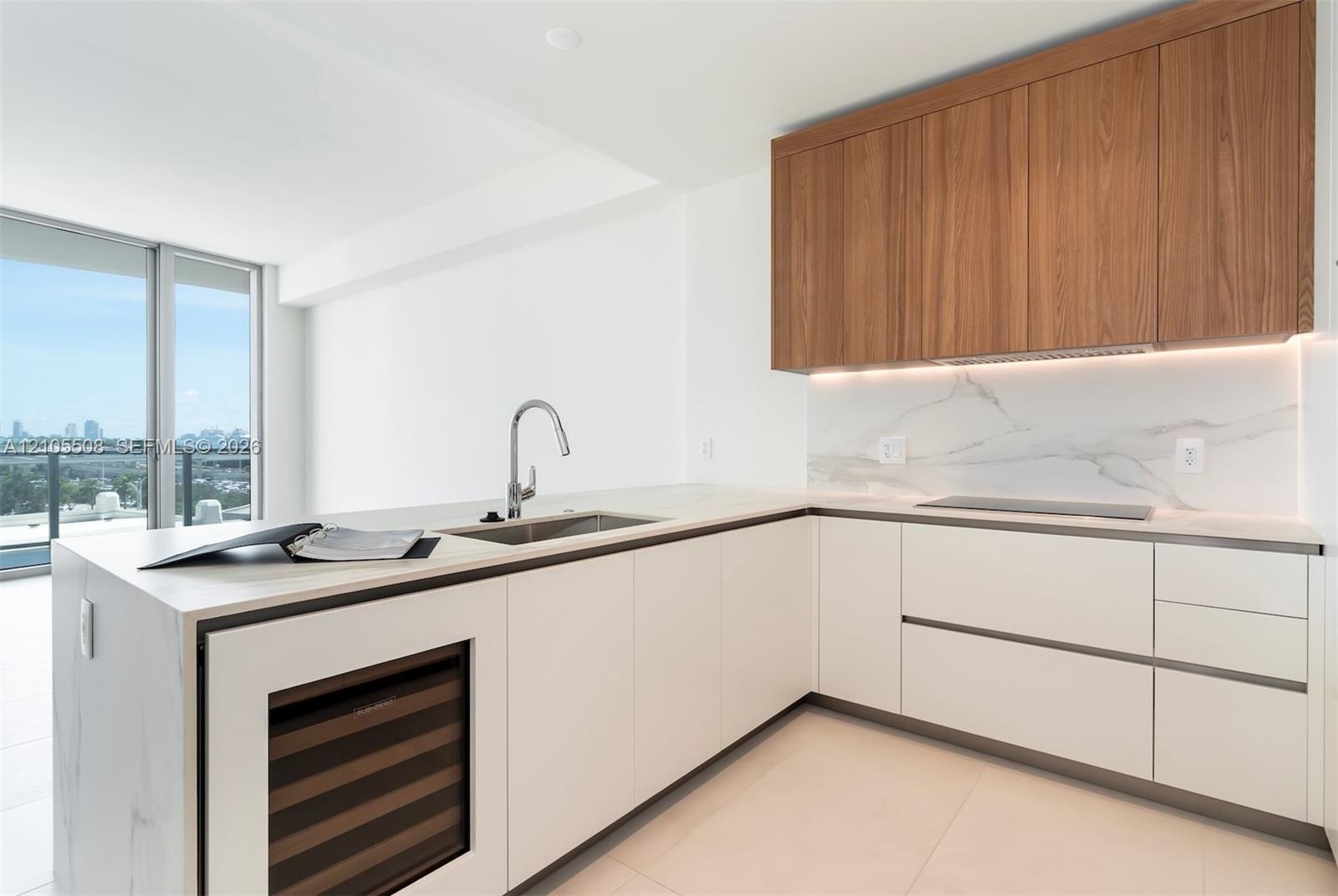 Modern kitchen featuring light wood-finish cabinetry, white flat-panel lower cabinetry, integrated stainless steel sink, under-cabinet lighting, and a