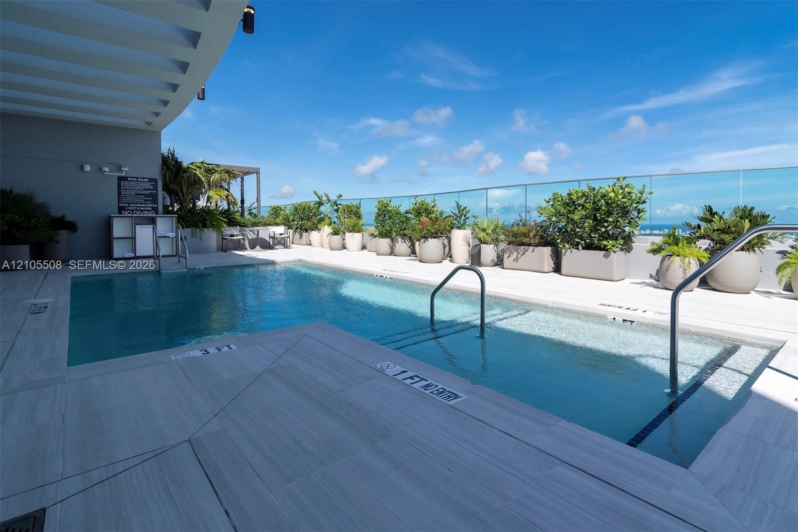 Rooftop swimming pool with integrated spa, glass safety barrier, and an array of potted plants
