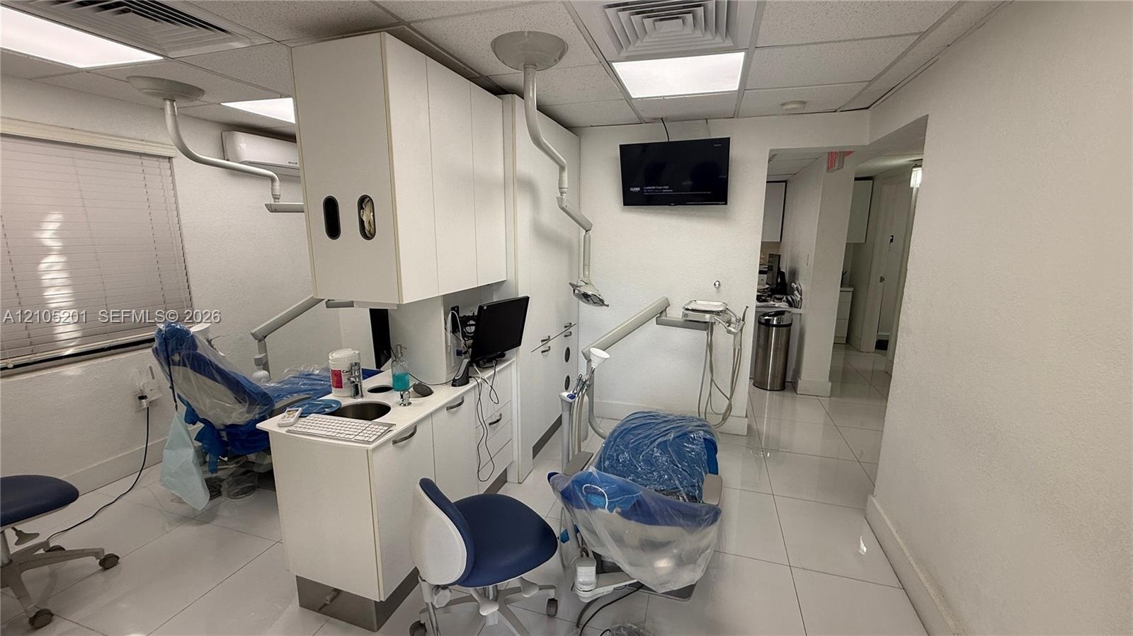 White tile flooring, built-in cabinetry, window with horizontal blinds, integrated lighting, and wall-mounted display