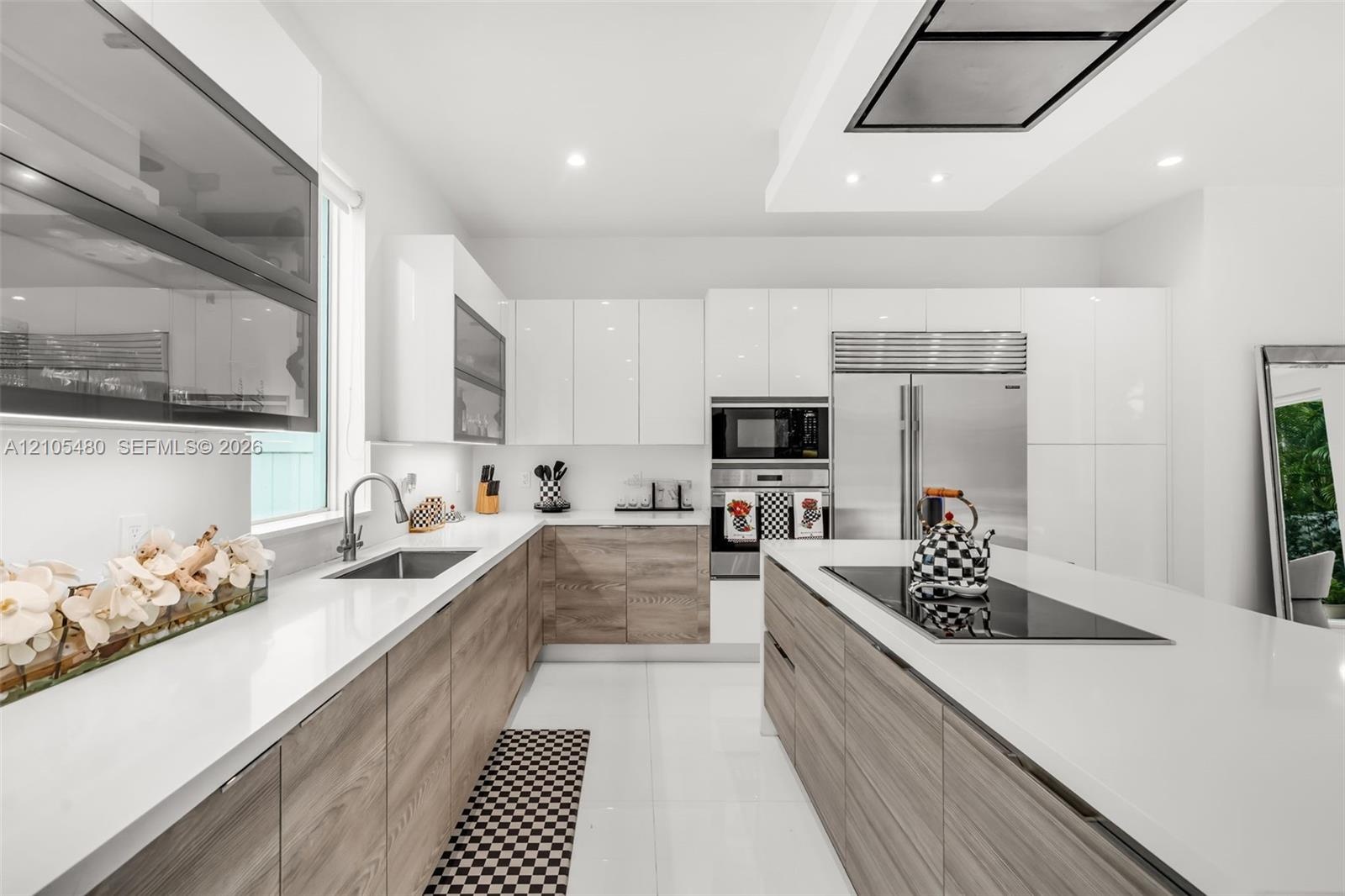 Modern kitchen featuring white glossy and wood-finish cabinetry, white countertops, stainless steel appliances, and an integrated cooktop on the islan