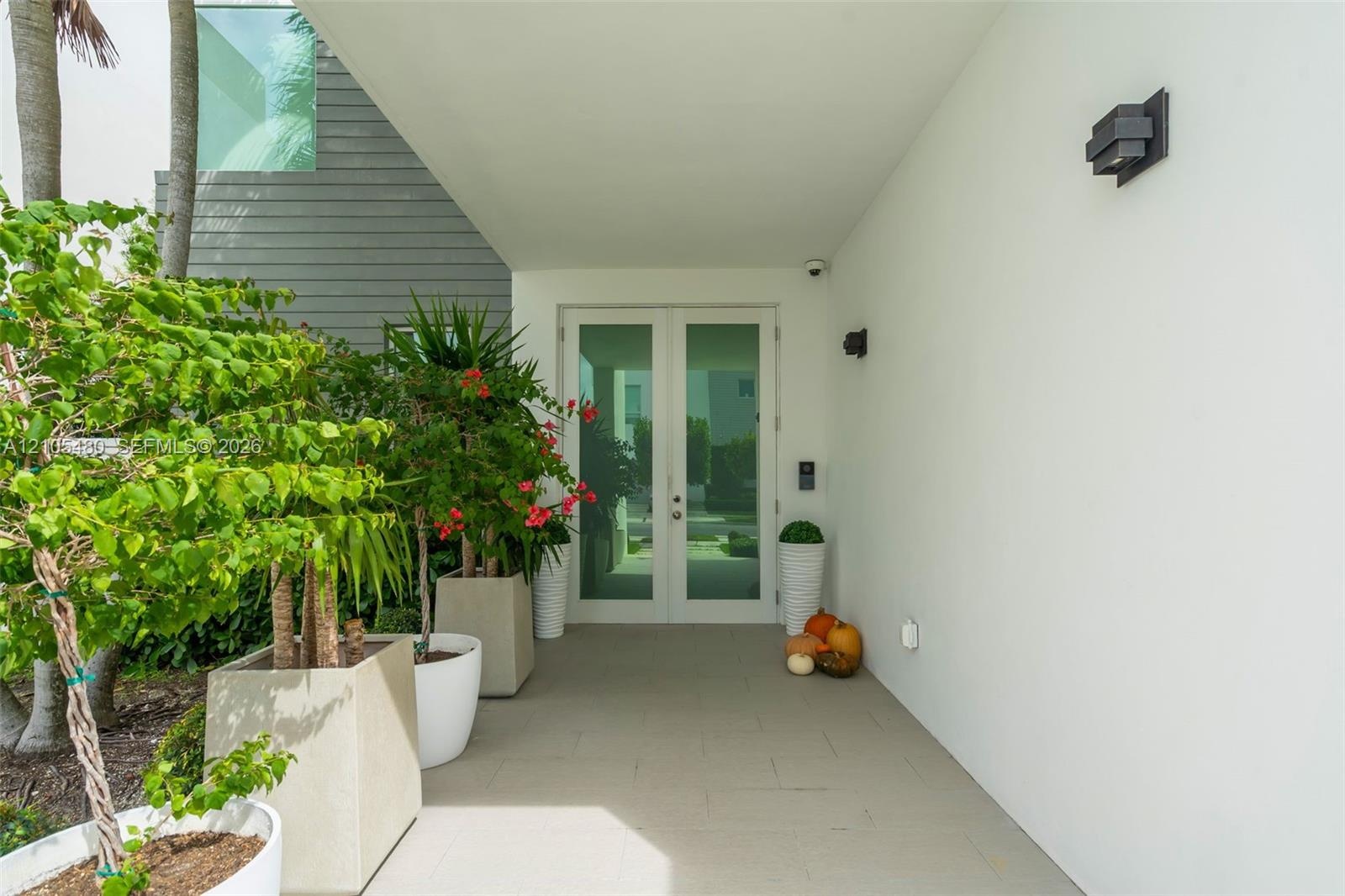 Covered entry featuring a light-toned concrete walkway, architectural wall sconces, and a modern double-door entry
