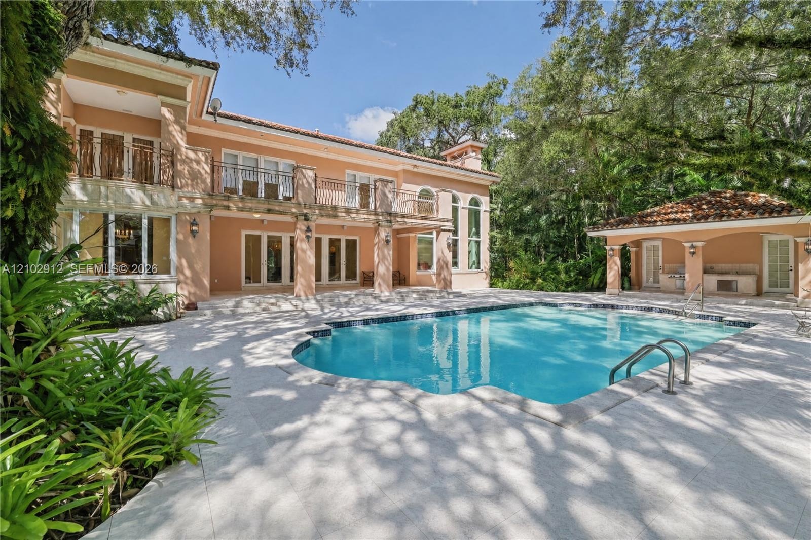 Expansive pool deck with a freeform swimming pool, outdoor kitchen, and a two-story residence featuring multiple balconies