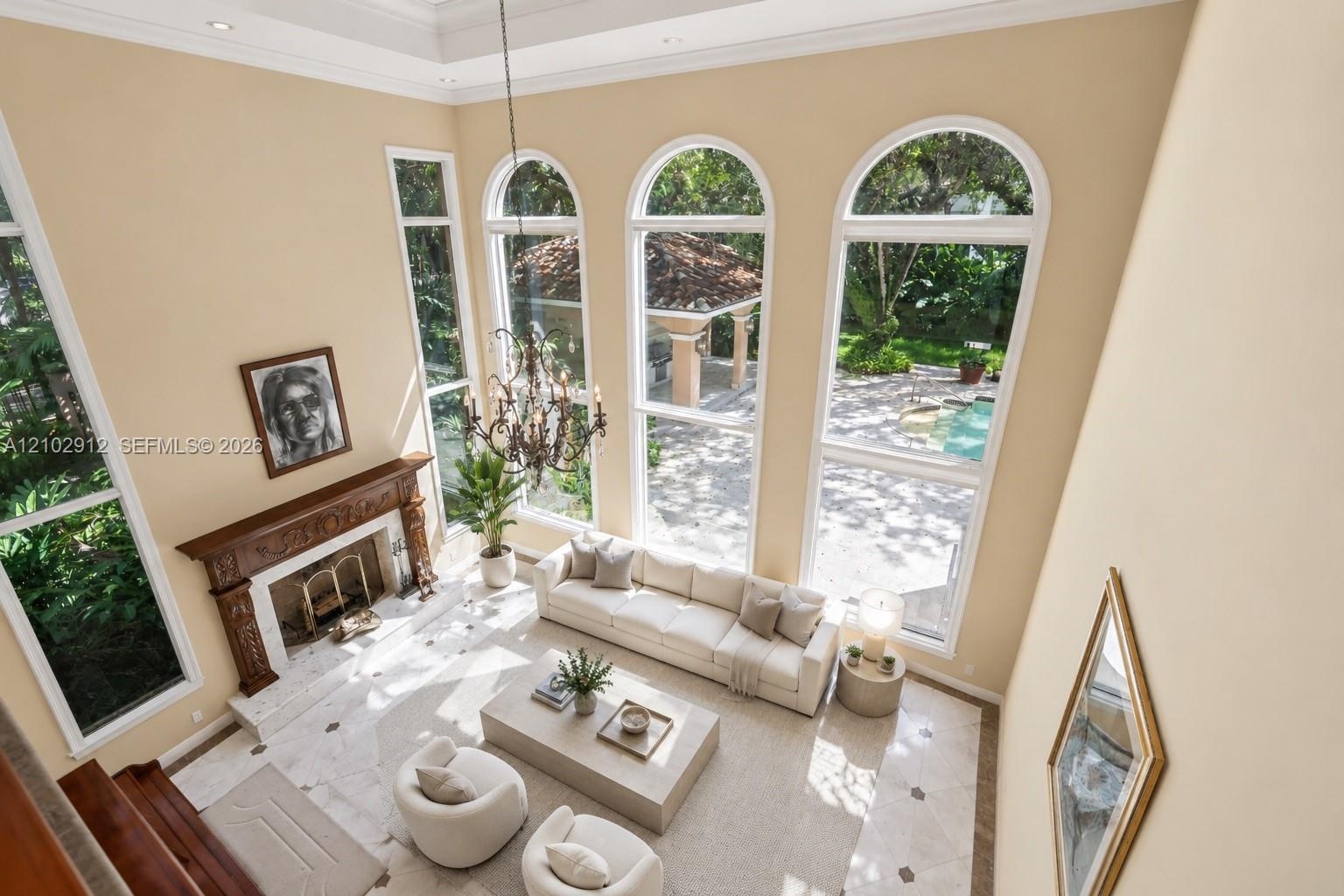Two-story living area with coffered ceiling, a decorative wood mantle fireplace, arched windows, and tiled flooring