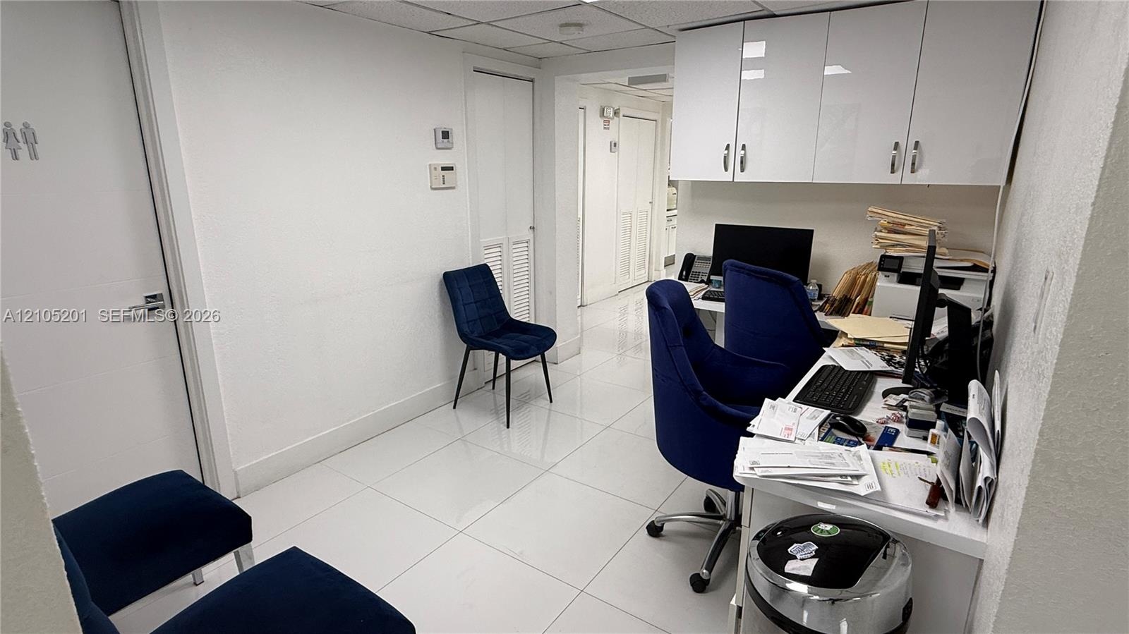 White tile flooring, built-in white cabinetry, white walls, and a white door with a silver handle