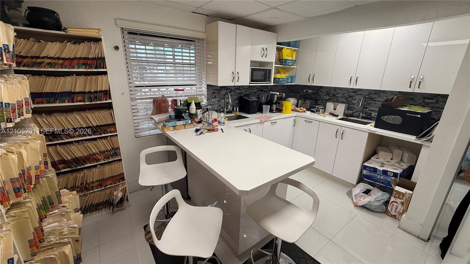 White cabinetry with modern hardware, dark tile backsplash, stainless steel sink with pull-down faucet, and white countertop island