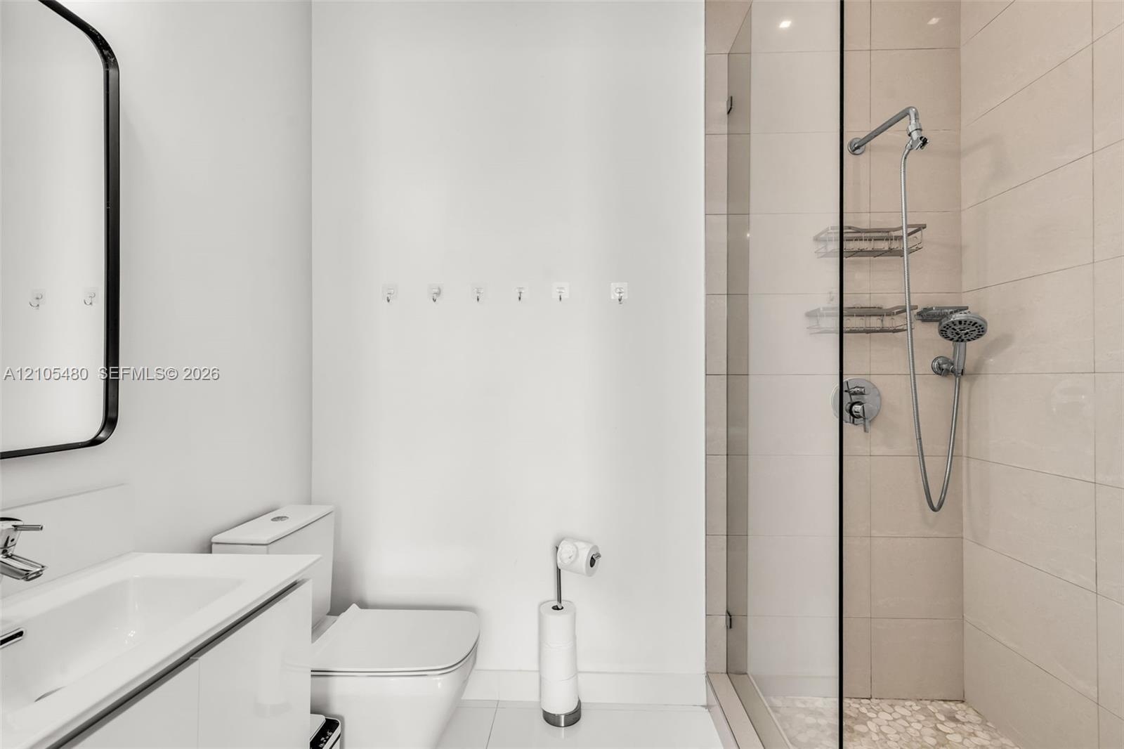 Modern vanity with integrated sink, sleek wall-mounted mirror, contemporary toilet, and a glass-enclosed shower with pebble-tiled flooring