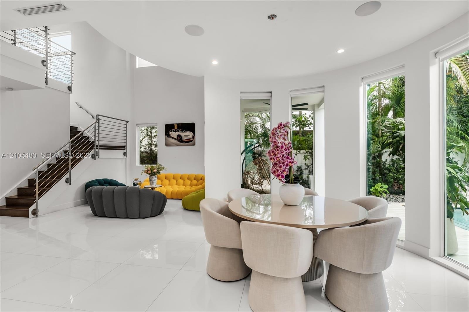 Curved architectural walls, high ceilings, large format tile flooring, wood-finish staircase with metal railings, and full-height windows