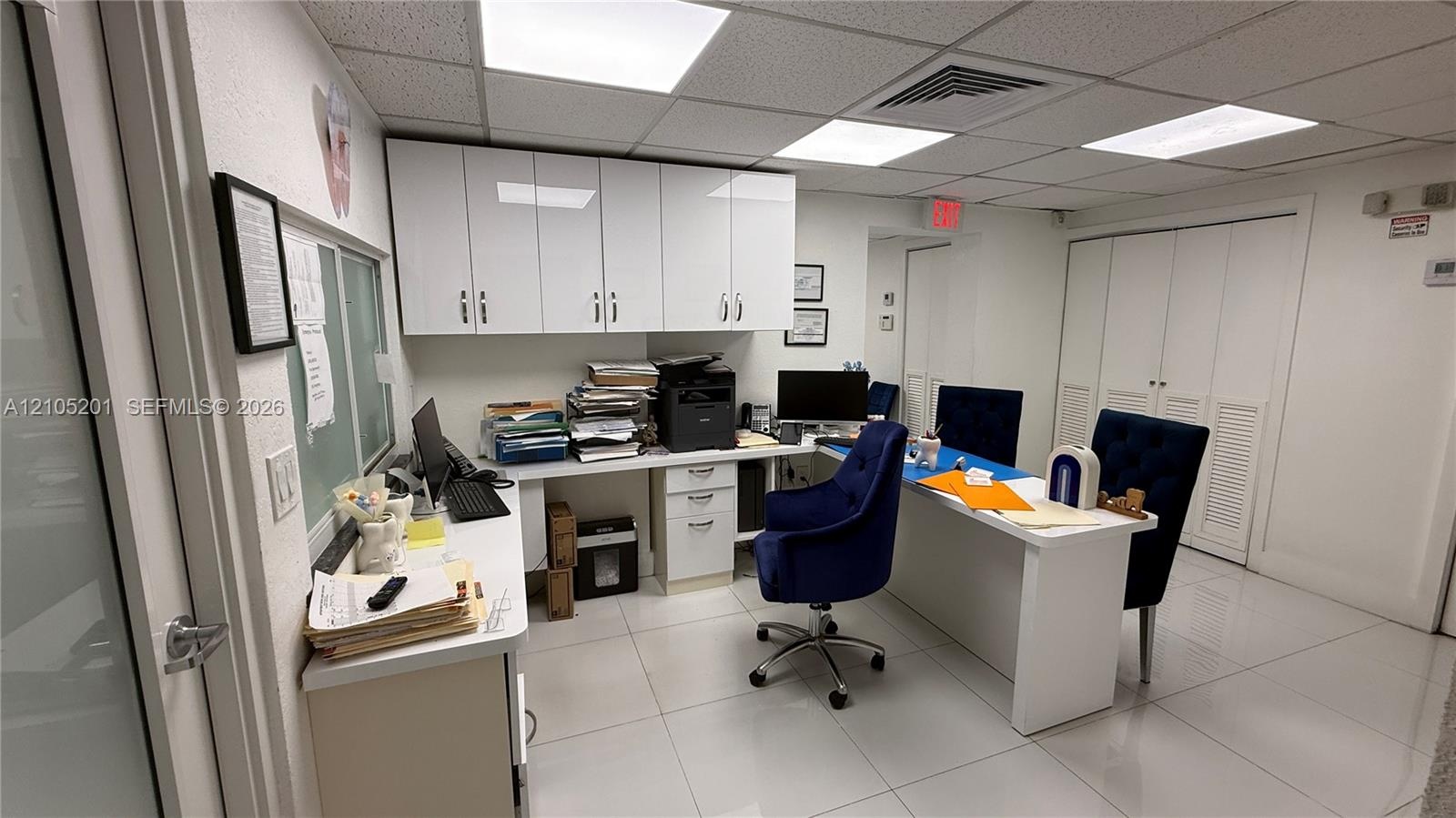 Recessed ceiling with integrated lighting, white wall-mounted cabinetry, built-in desk with integrated storage, white tile flooring, and louvered clos