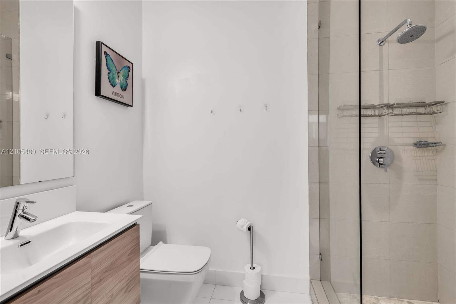 Bathroom featuring a floating wood-finish vanity, integrated rectangular sink, wall-mounted mirror, and a glass-enclosed shower with a rainfall shower