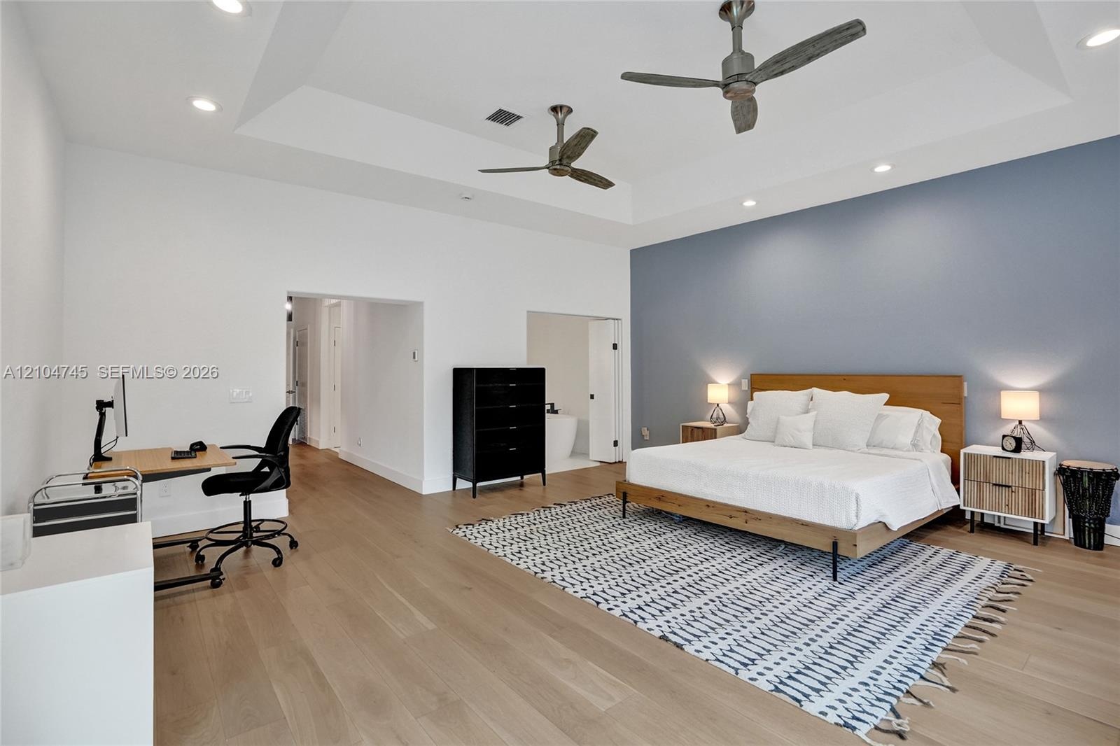 Tray ceiling with recessed lighting, two ceiling fans, wood-finish flooring, and a distinct accent wall