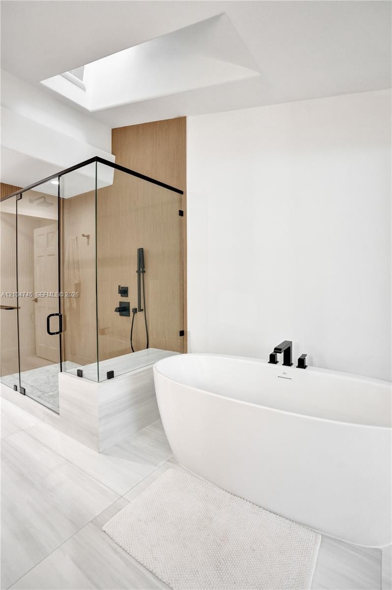 Freestanding soaking tub with matte black fixtures, glass-enclosed shower with matte black shower system, and skylight