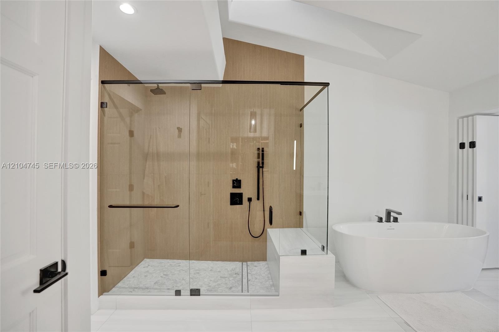 Spacious shower enclosure with glass panels, light wood-finish wall, and black fixtures