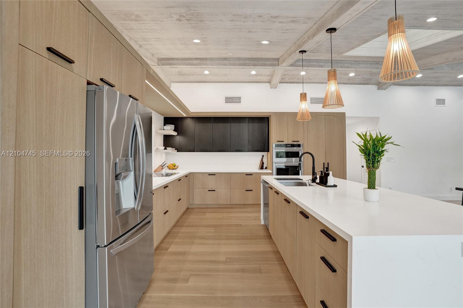 Spacious kitchen featuring light wood-finish cabinetry, stainless steel appliances, a large center island with a sink, white countertops, and wood-fin