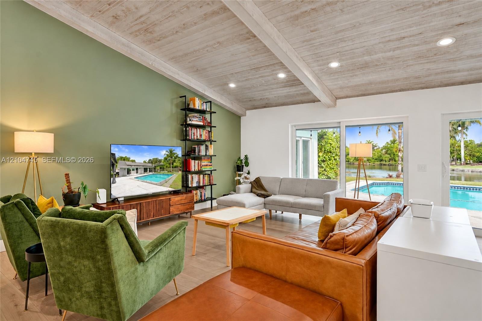 Vaulted wood-plank ceiling with exposed beams, recessed lighting, expansive sliding glass doors, wood-finish flooring, and a built-in shelving unit