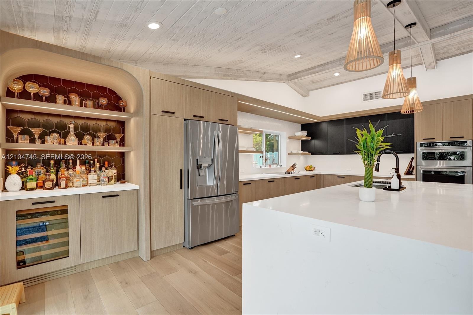 Kitchen featuring wood-finish flooring, white vaulted ceiling with exposed beams, light wood-finish cabinetry, a large kitchen island with a white cou