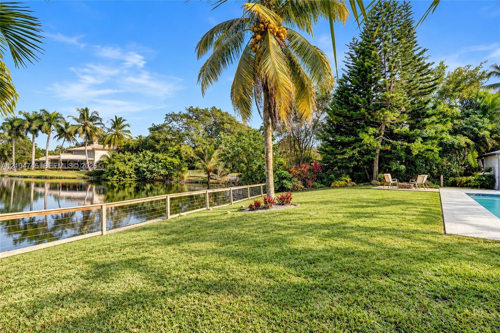 Expansive lawn with mature landscaping, cable railing fence, and a visible pool area