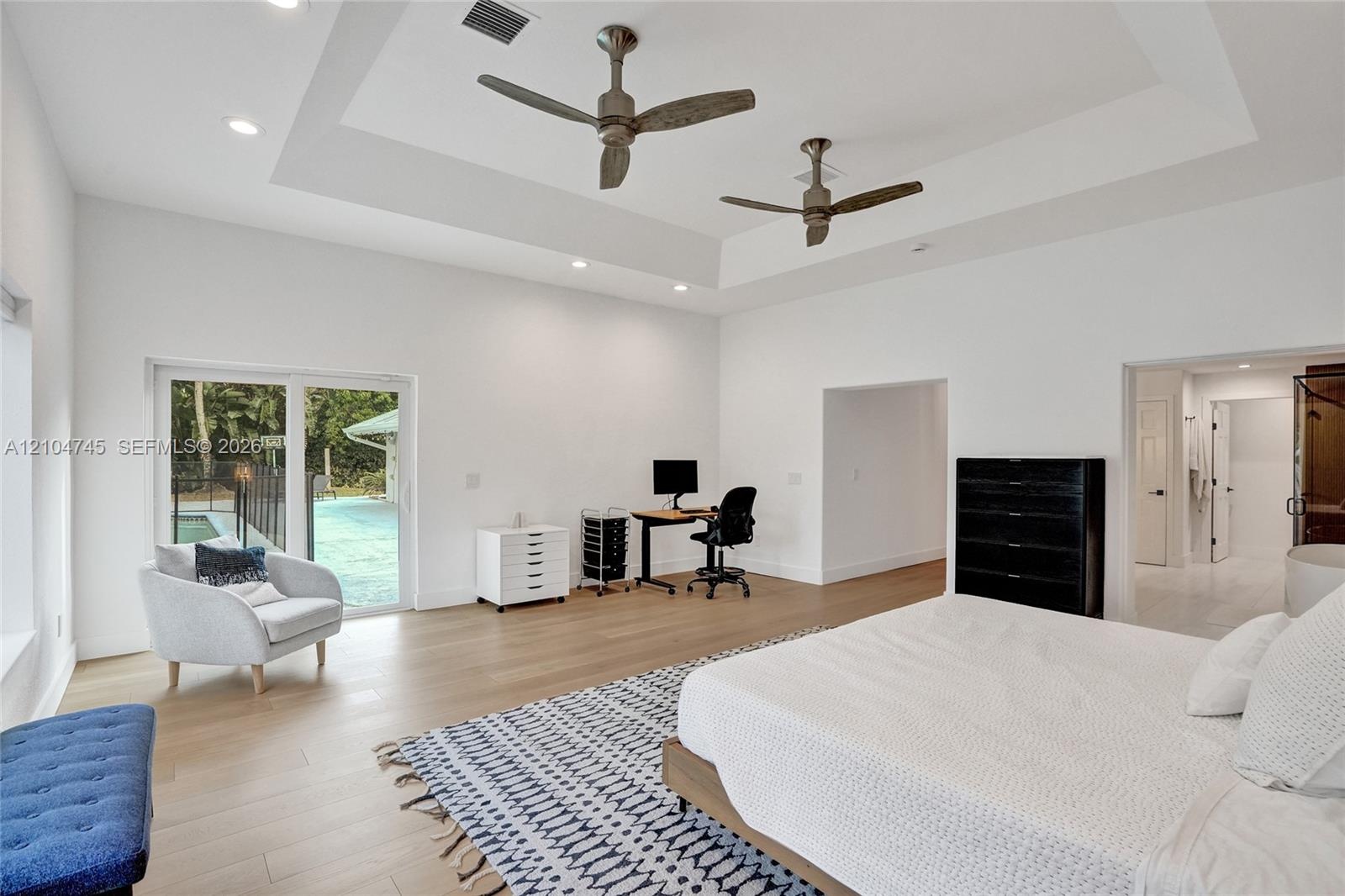 Recessed tray ceiling with integrated lighting, wood-finish flooring, dual ceiling fans, and sliding glass door