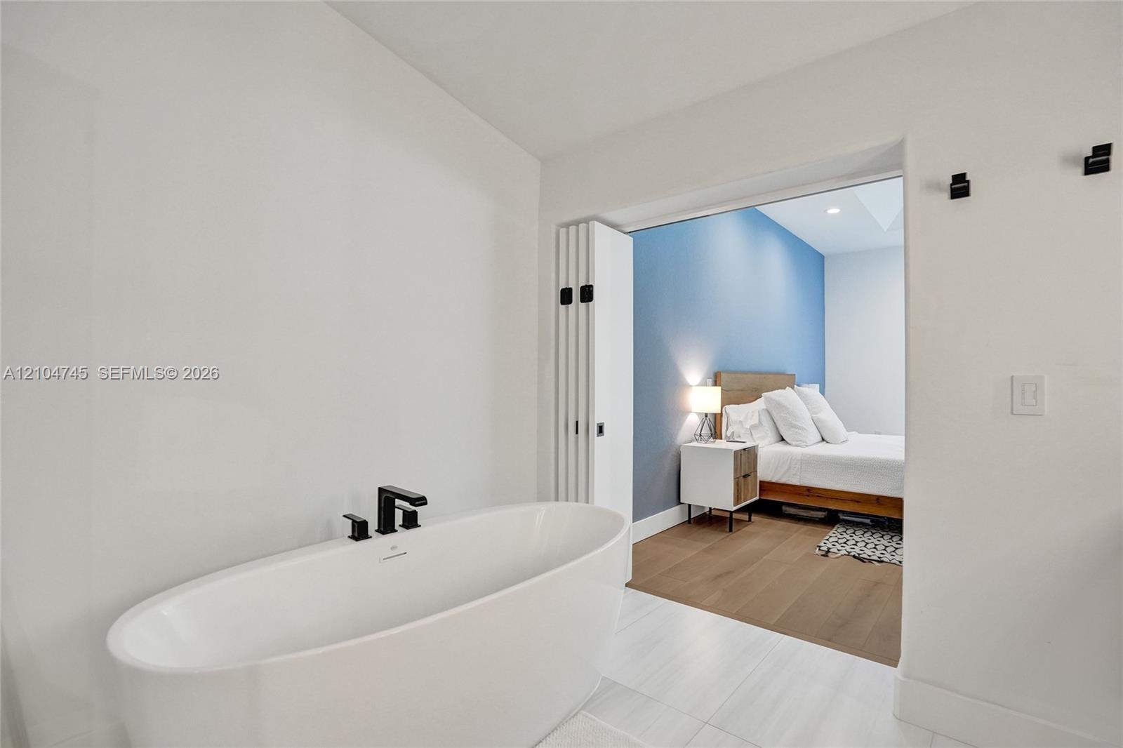 Freestanding soaking tub with matte black fixtures, white tile flooring, and a wide entryway