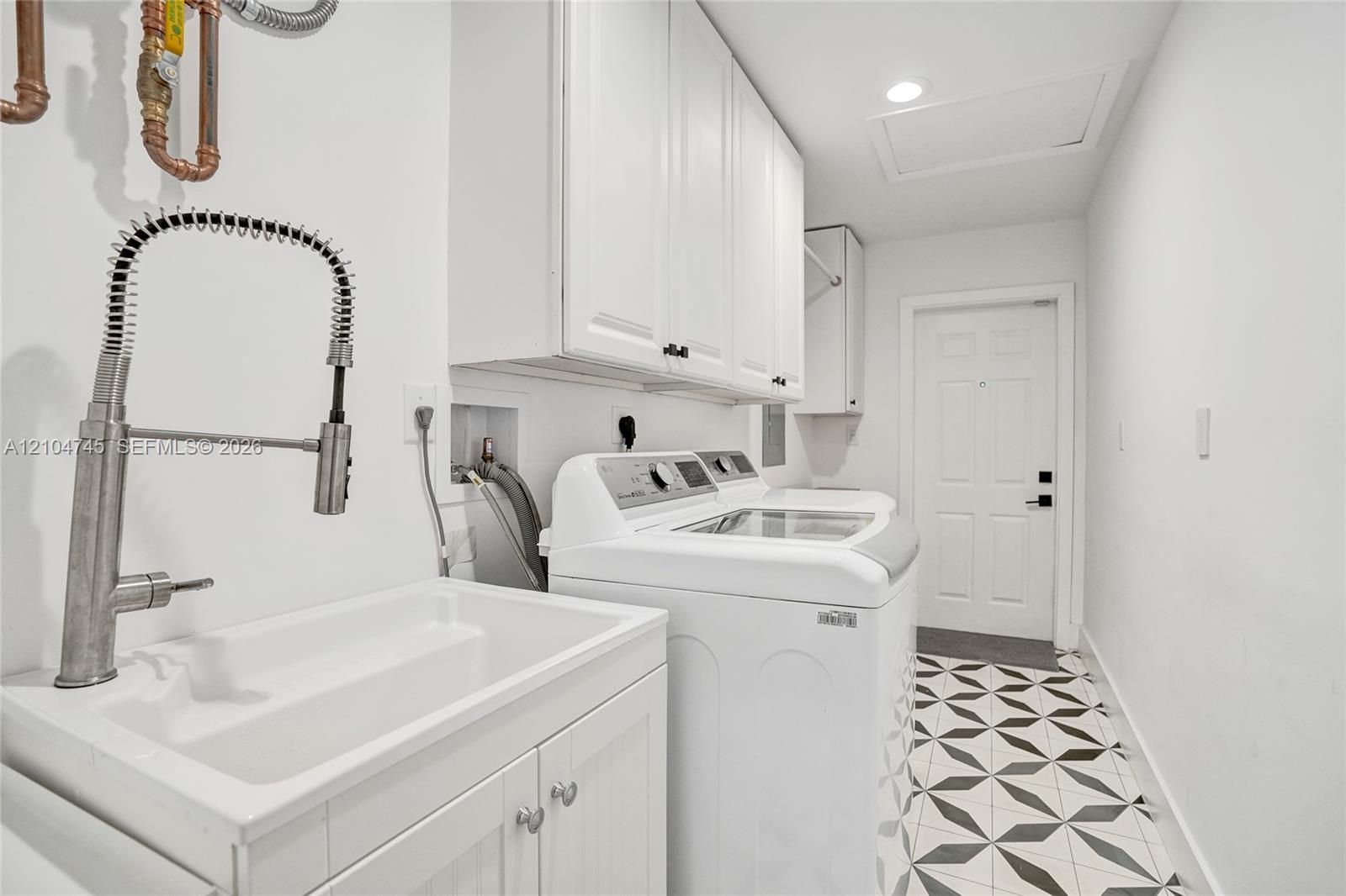 Utility room featuring a built-in sink with a pull-down faucet, upper and lower cabinetry, a patterned tile floor, and a flush-mount ceiling light
