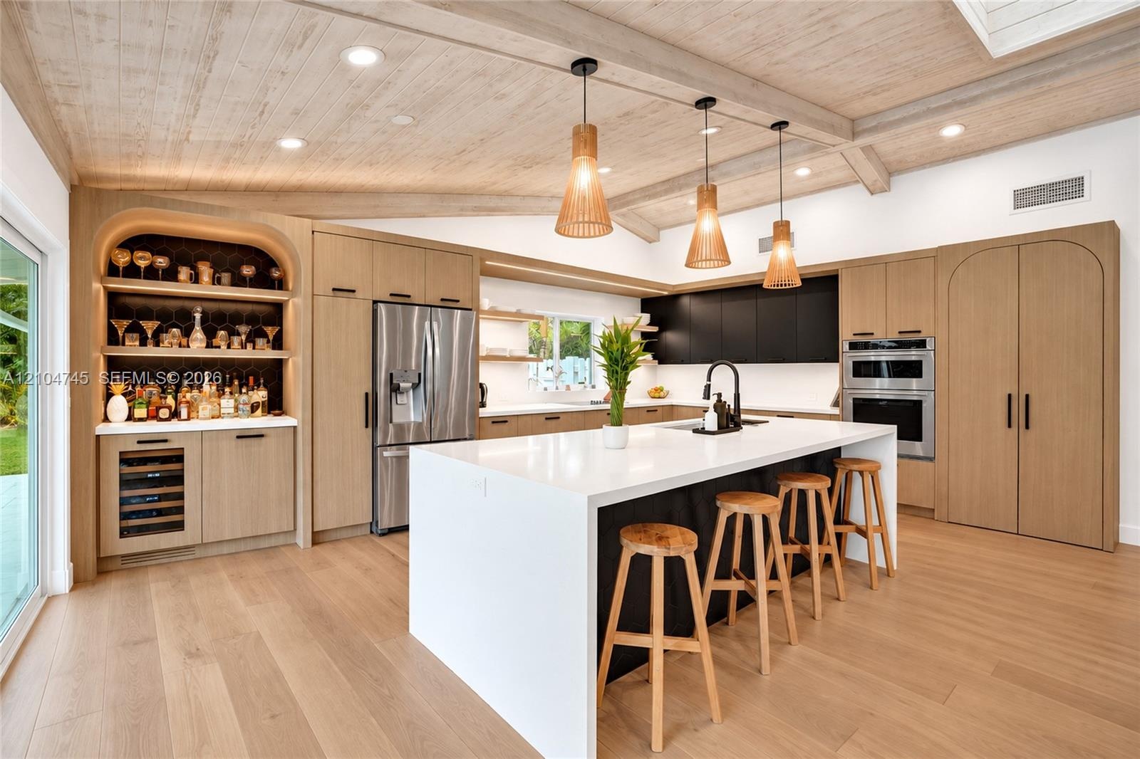 Vaulted wood-finish ceiling with exposed beams, wood-finish flooring, stainless steel appliances, built-in shelving with integrated lighting, and a ki