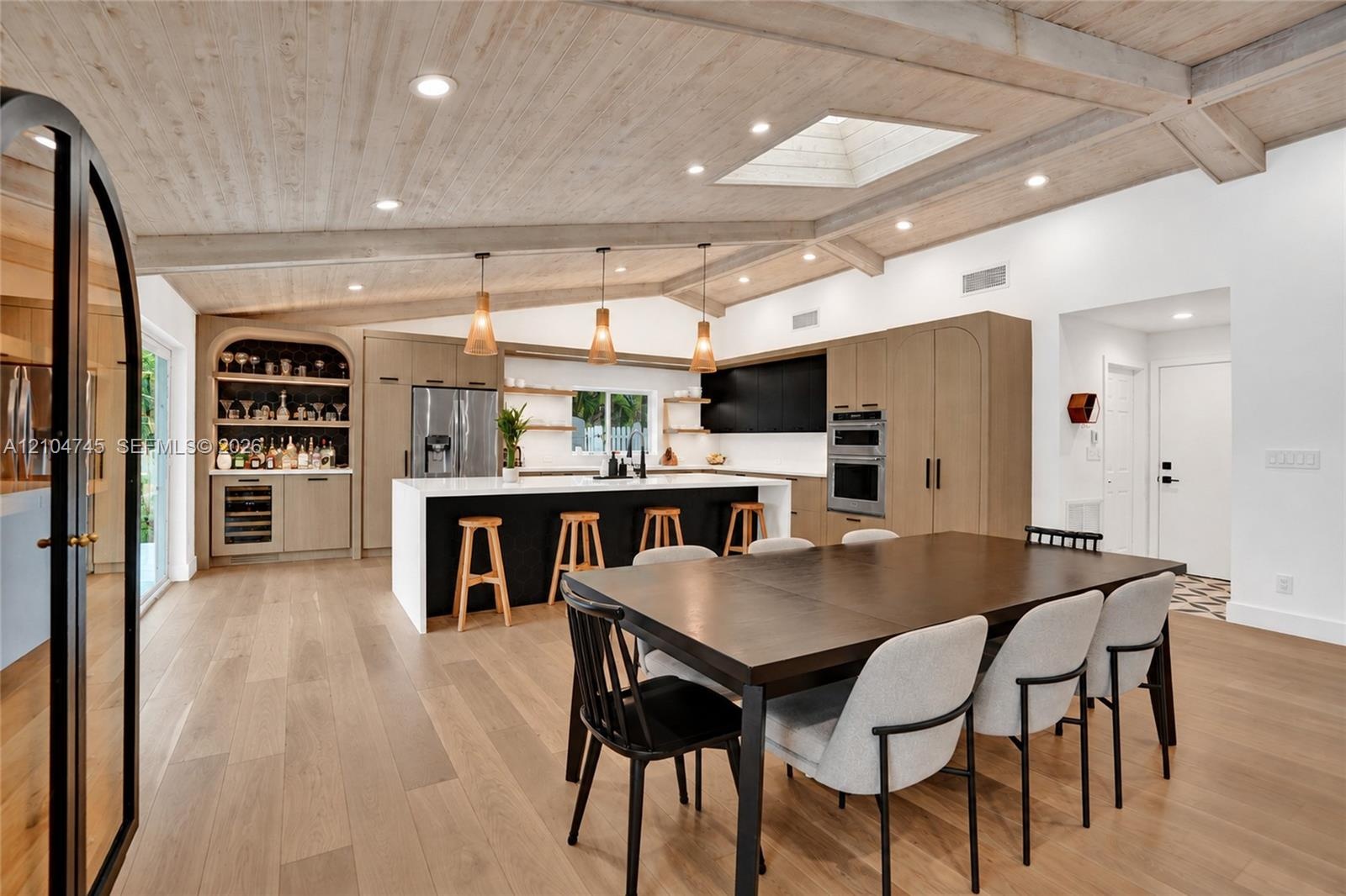 Vaulted wood-finish ceiling with exposed beams, wood-finish flooring, custom built-in bar, center island with stone countertop, and integrated stainle