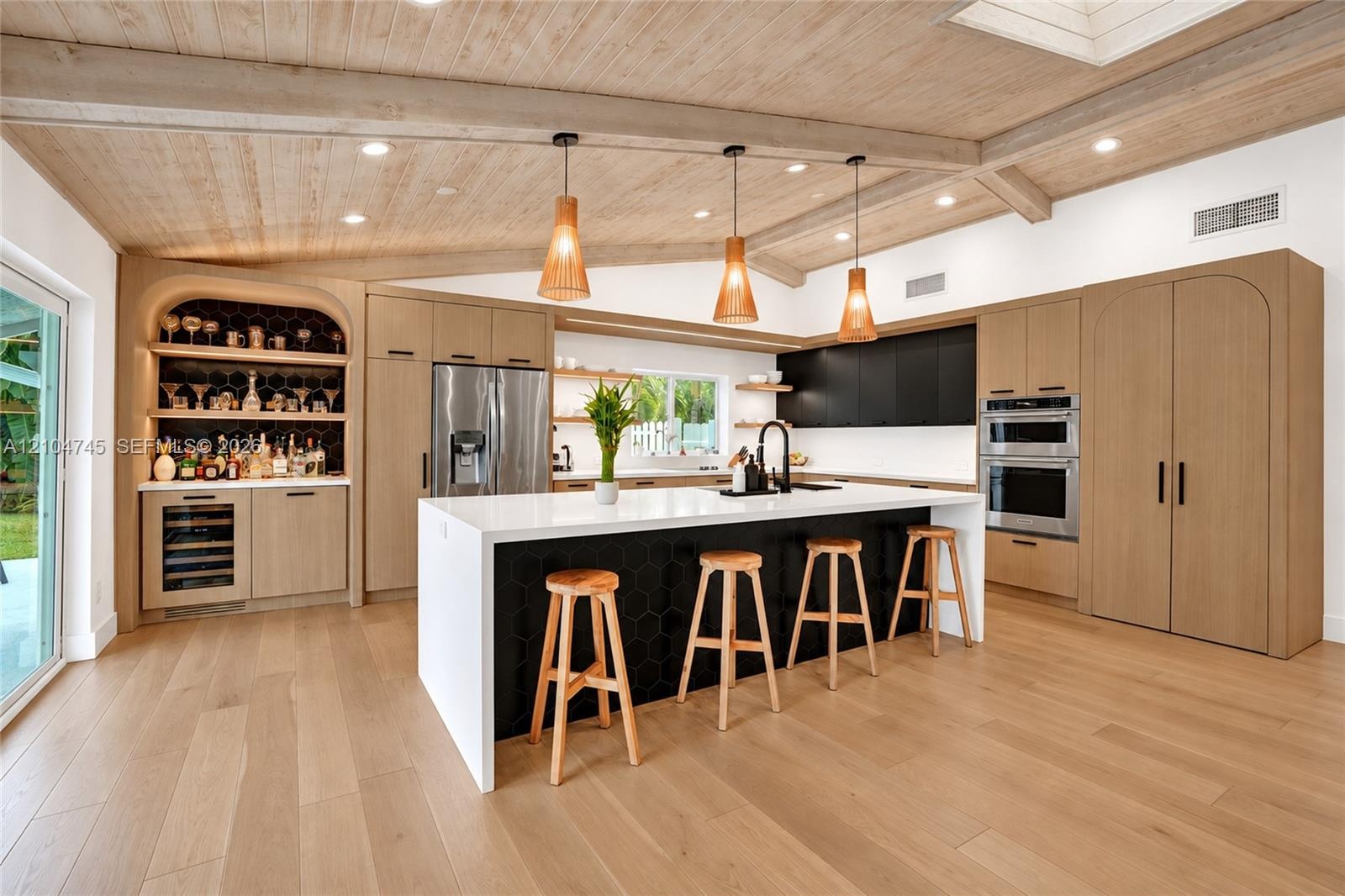 Expansive kitchen featuring a large island, wood-finish flooring, custom cabinetry, integrated appliances, and a built-in bar with beverage refrigerat