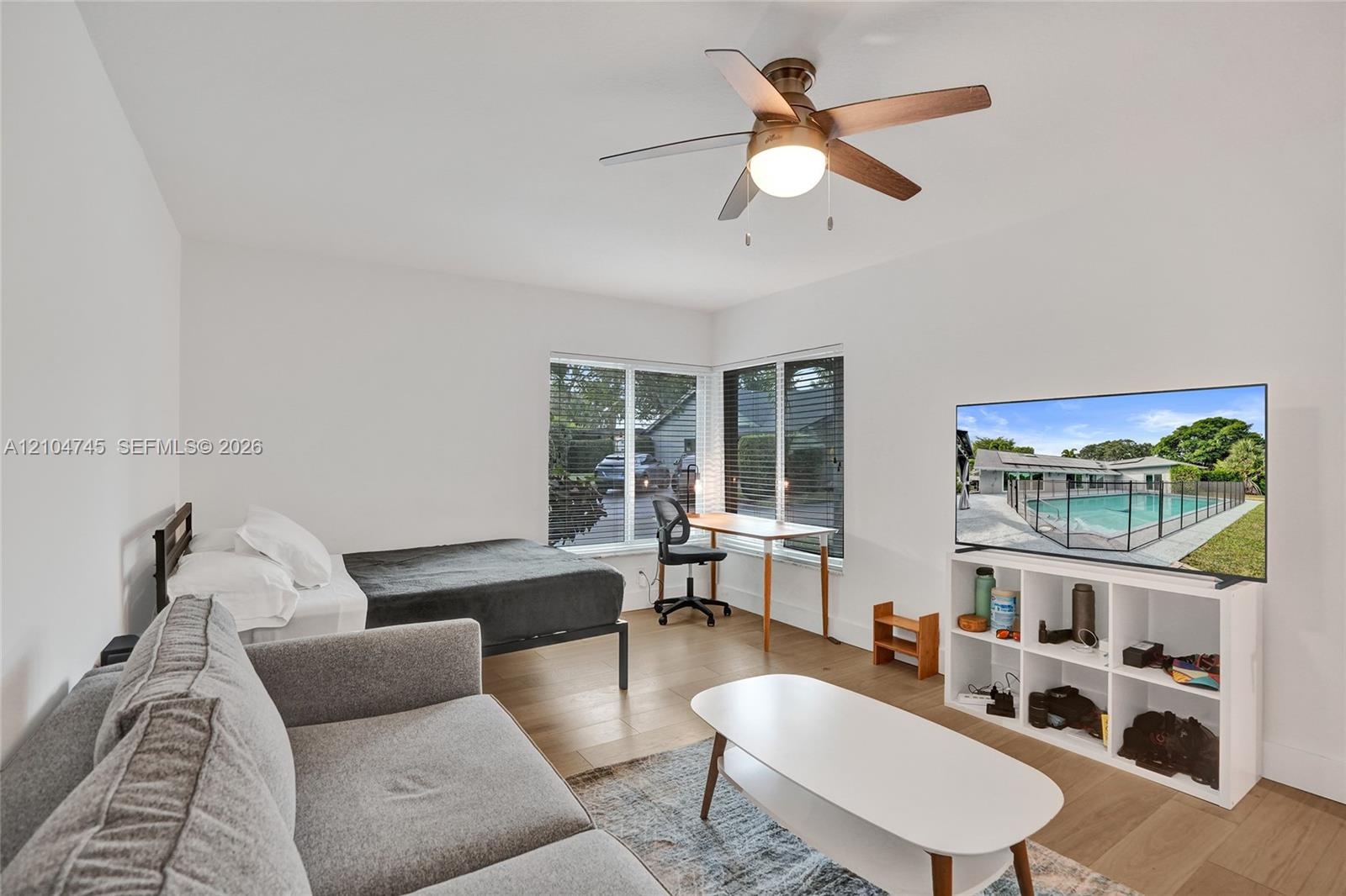 Hardwood-finish flooring, corner windows with blinds, recessed lighting, ceiling fan with integrated light, and a white storage unit