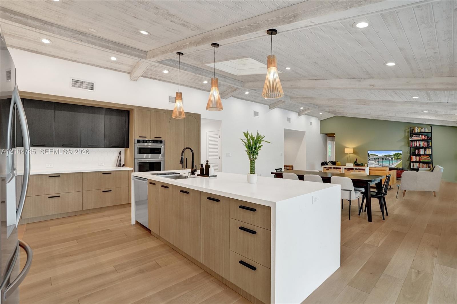 Open-concept kitchen featuring an expansive island with a white countertop, wood-finish cabinetry, and built-in stainless steel appliances