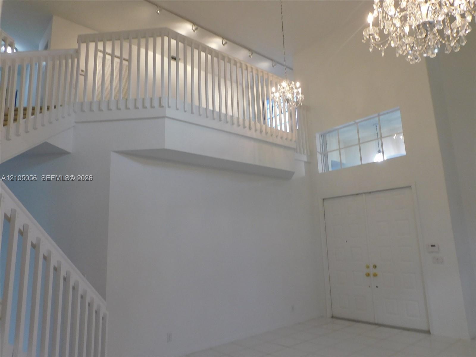 Two-story foyer featuring a double staircase with white balusters, two crystal chandeliers, and loft overlooks social areas - loft is an added bonus t
