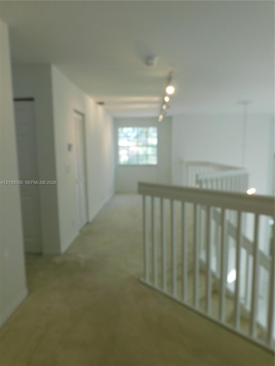 Staircase featuring white wood railings and carpeted treads, with tile flooring at the base and leading to upstairs bedrooms and loft.