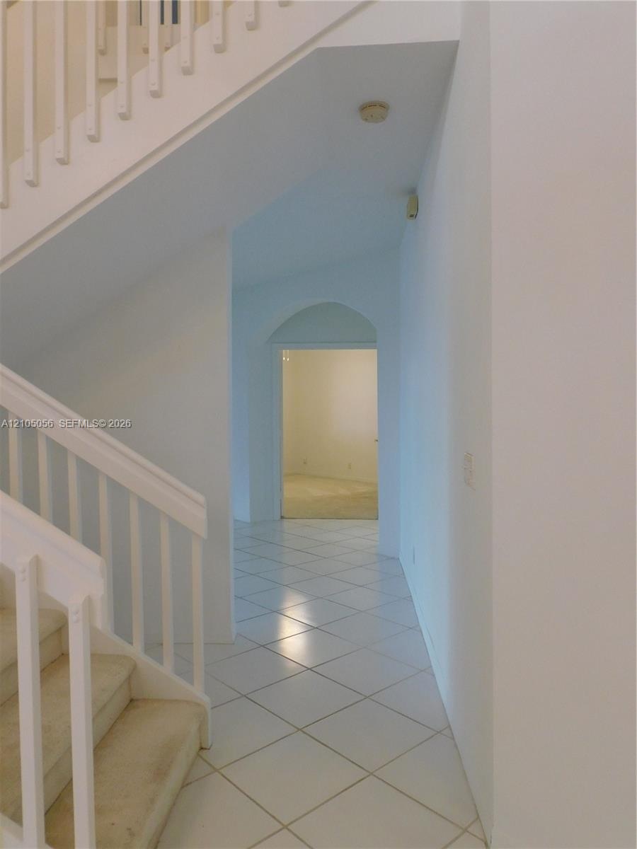 Two-story foyer with a bifurcated staircase featuring white railings, carpeted treads, and tiled flooring